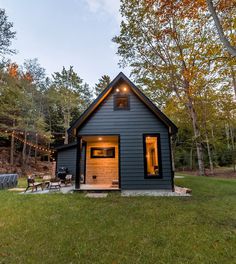 a small house with lights on the front door and windows in the back yard, surrounded by trees