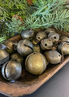 there are many bells in the tray on the table next to pine cones and evergreen branches