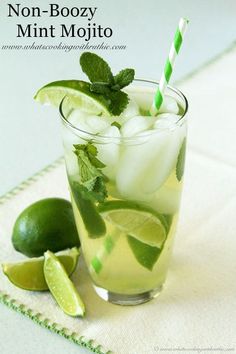 a glass filled with ice, lime and mint on top of a table next to sliced limes