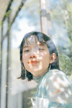 a young woman standing in front of a tree and looking up at the sky with her eyes closed