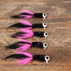 four black and pink feathers are on a wooden surface, with white bead eyes