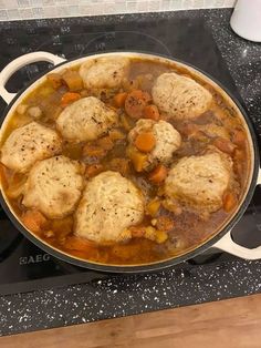 a pot filled with stew and dumplings sitting on top of a stove burner