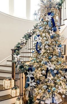 a decorated christmas tree with blue and white ornaments on the top is in front of a staircase