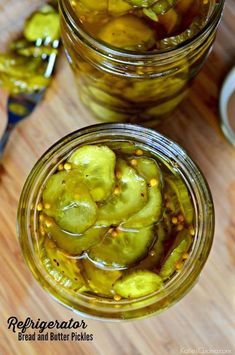 two jars filled with pickles sitting on top of a wooden table next to spoons