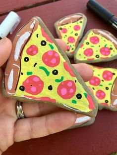 a hand holding a piece of painted rock shaped like a slice of pizza