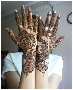 two hands with henna designs on them and a clock in the backround