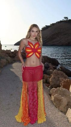 a beautiful woman in a red and yellow outfit standing on the beach with her hands on her hips