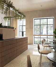 a coffee shop with tables, chairs and plants hanging from the ceiling in front of large windows