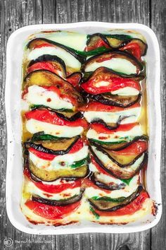 a white dish filled with vegetables covered in cheese and sauce on top of a wooden table