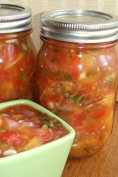 two jars filled with food sitting on top of a wooden table next to a green bowl