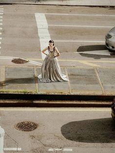 a woman in a long dress standing on the side of a road next to cars