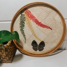 a plant sits next to a wooden frame with an embroidered design on it and a potted plant in the foreground