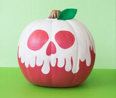 a painted pumpkin sitting on top of a green table next to a white and red apple