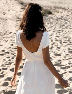 a woman in a white dress walking on the beach with her back to the camera