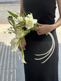 a woman in a black dress holding a bouquet of flowers and pearls on her belt