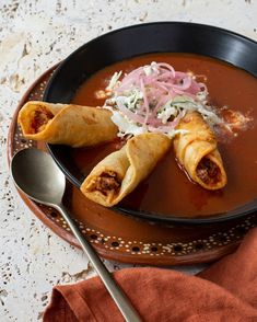 a black bowl filled with soup and some food on top of a table next to a spoon