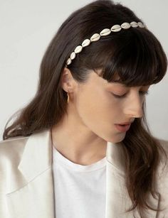 a woman wearing a white blazer jacket and gold earring with pearls on her head