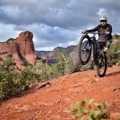 a man riding a mountain bike on top of a red dirt hill with mountains in the background