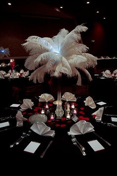 the table is set with black and white linens, silverware, and feathers