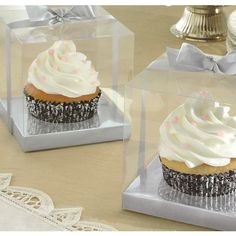 two cupcakes with white frosting and sprinkles in clear boxes