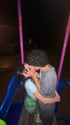 two people hugging each other on a swing ride at night with lights in the background