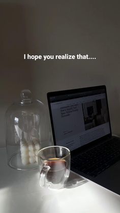 a laptop computer sitting on top of a white table next to a glass cup filled with liquid