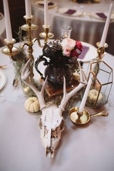 a table topped with candles and a vase filled with flowers next to a deer skull