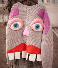 an ugly sweater hanging on a tree with blue eyes and pink nose, which is shaped like a monster's head