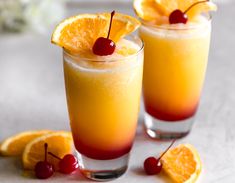 two glasses filled with orange juice and garnished with cherries