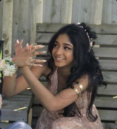 a woman sitting on top of a wooden bench holding her hands up in the air