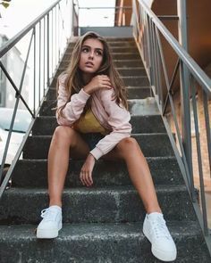 a woman is sitting on the stairs with her legs crossed and looking at the camera