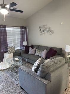 a living room with gray couches and purple pillows on the carpeted flooring