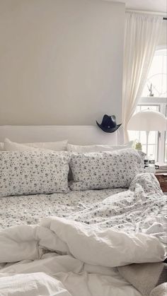 an unmade bed with white sheets and blue flowers on the comforter is in front of a window