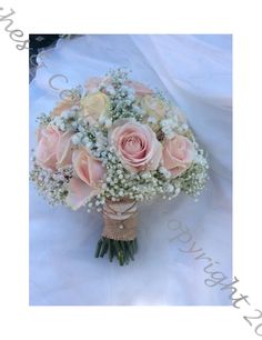 a bridal bouquet with pink roses and baby's breath in it on a white cloth