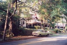 an old green car parked in front of a house on the side of a road