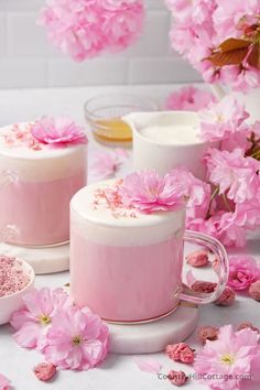 some pink flowers are on the table next to two jars and spoons with powder in them