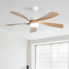 a ceiling fan with wooden blades in a white room next to a window and chair