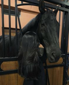 a woman standing next to a black horse in a stall with its head over the gate