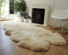 a large white sheepskin rug in front of a fireplace with potted plants on the floor