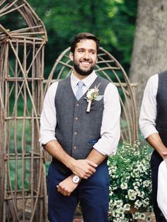 two men standing next to each other in front of a wooden structure with flowers on it