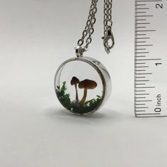 a small glass pendant with two mushrooms in the forest on it's side, next to a measuring ruler