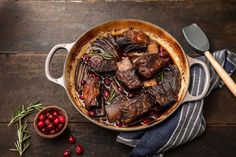 a pot filled with meat and cranberries on top of a wooden table next to a