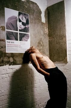 a shirtless man leaning against a brick wall in front of a poster on the wall