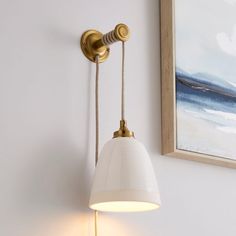 a white lamp hanging from the side of a wall next to a painting on the wall