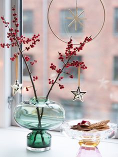 a glass vase filled with red berries next to a star decoration on a window sill