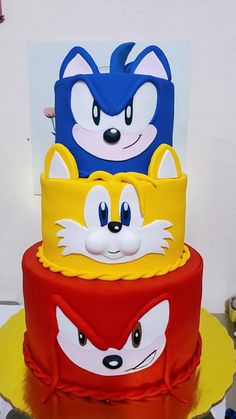 three tiered cake decorated with cartoon characters on top of each other in red, yellow and blue