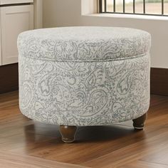 a round ottoman sitting on top of a hard wood floor next to an open window