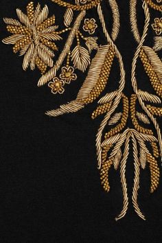 an embroidered design on black fabric with gold flowers and leaves in the center, as well as other decorative details