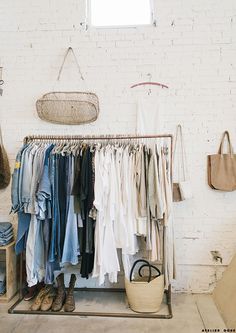 a rack with clothes and shoes hanging on it in front of a white brick wall