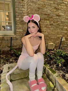 a woman in pink is sitting on steps with her legs crossed and wearing mouse ears